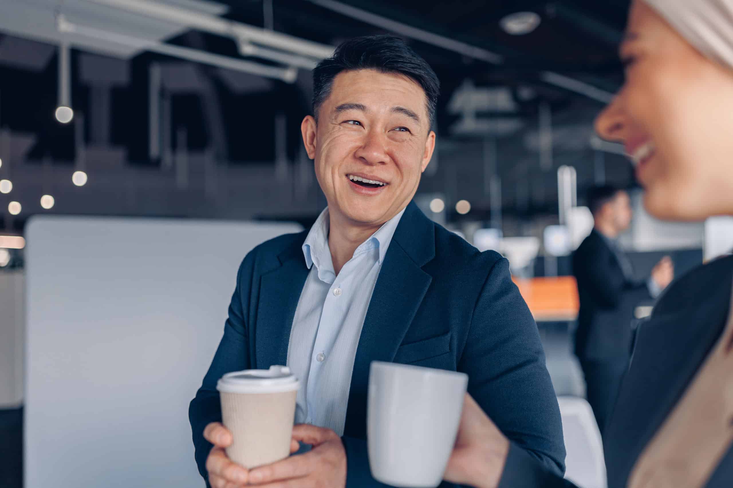 Zwei glückliche multikulturelle Kollegen, die während der Pause im Büro sprechen und Kaffee trinken