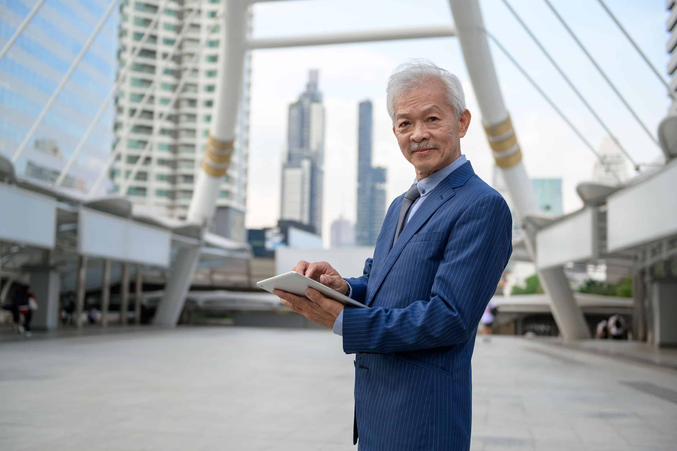 Erfahrener asiatischer Geschäftsmann, der ein Tablet in einer modernen Stadt benutzt