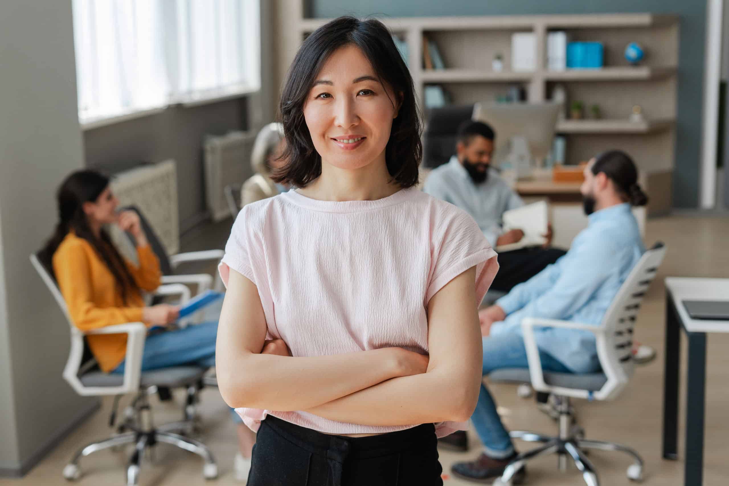 Selbstbewusste asiatische Geschäftsfrau, die in einem modernen Büro mit einem vielfältigen Team lächelt