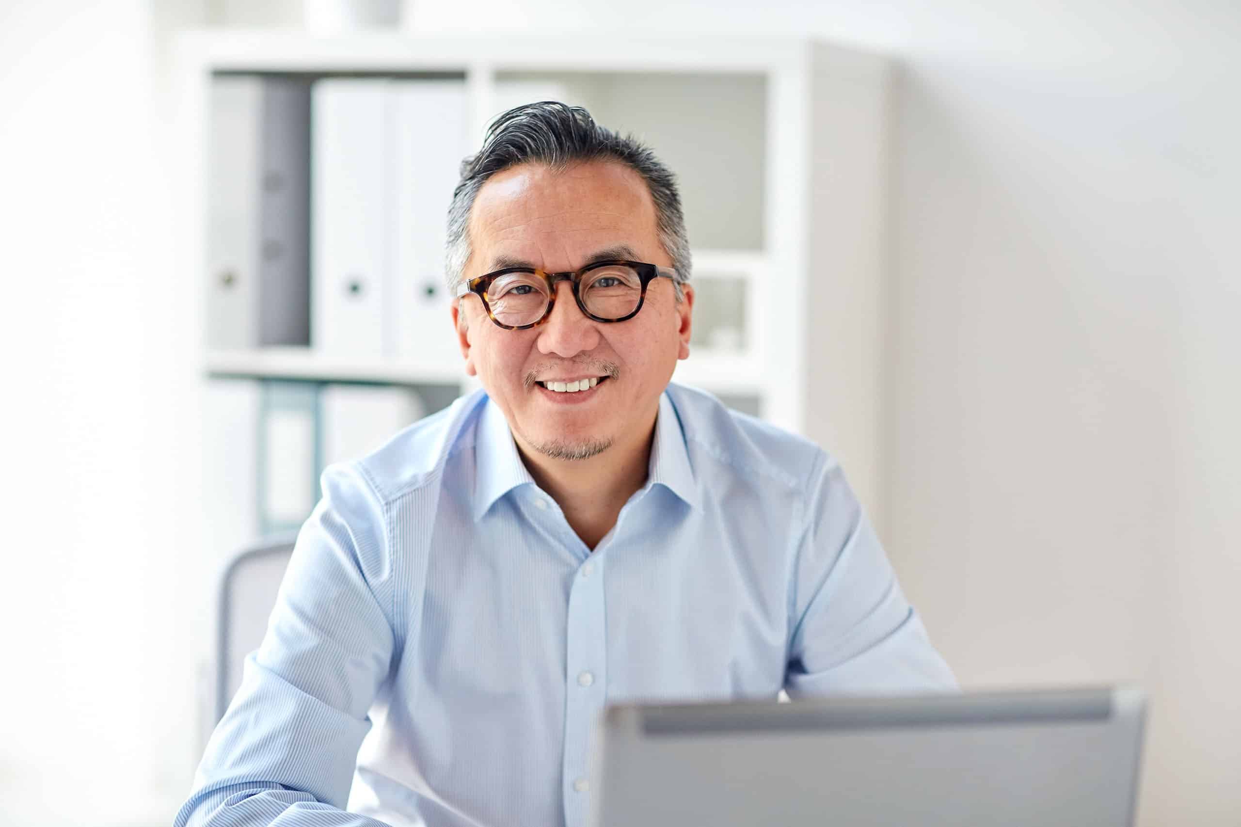 Glücklicher Geschäftsmann mit Brille und Laptop im Büro